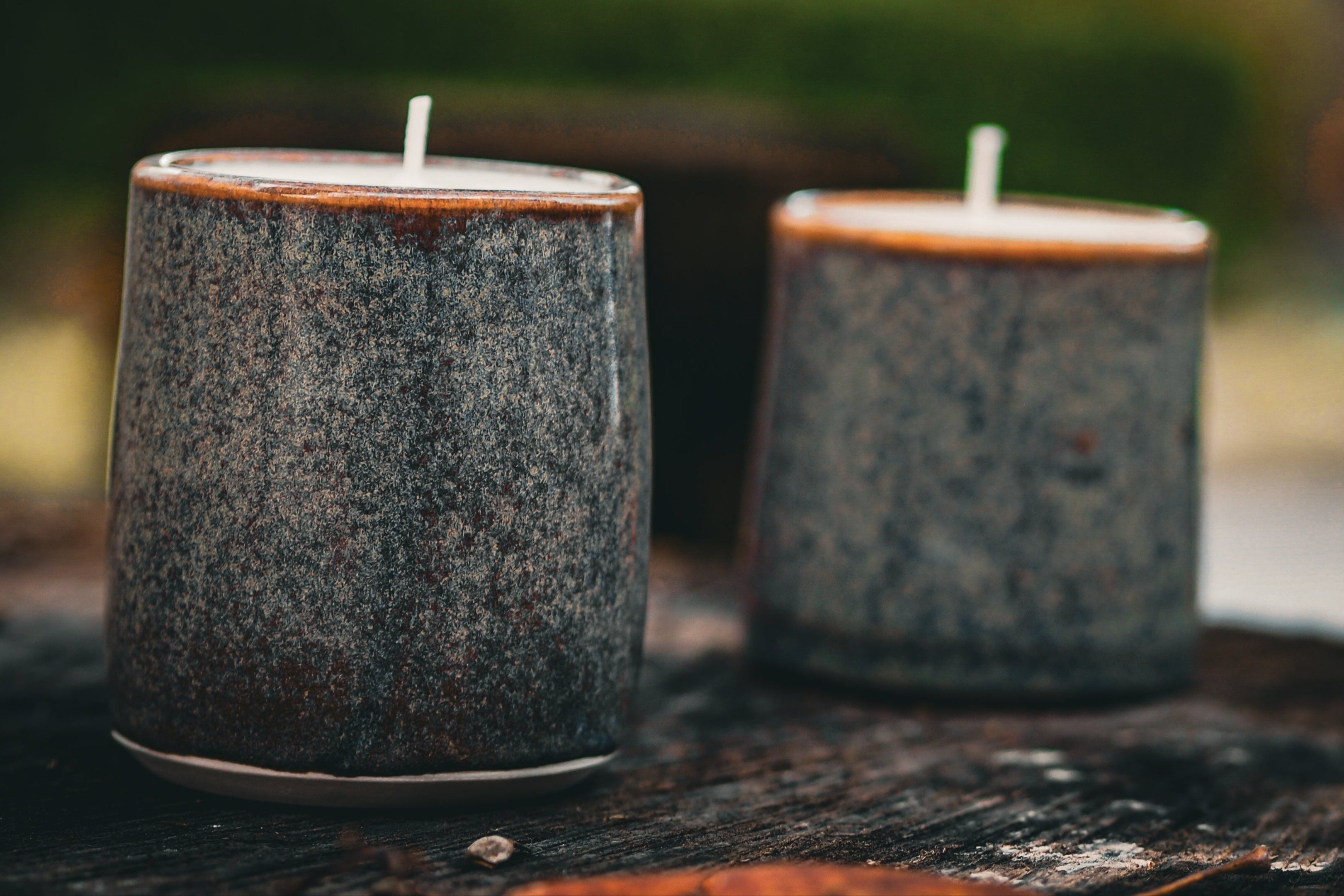 Two speckled gray candles on a wooden surface with a blurred natural background