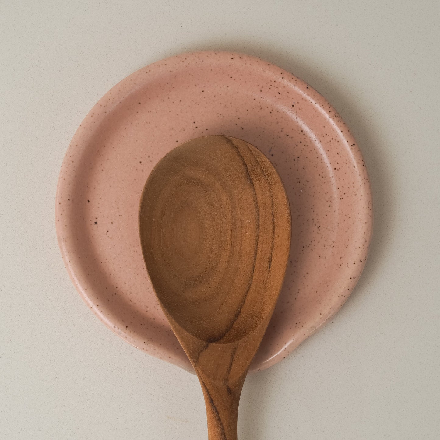 Wooden spoon on a pink ceramic spoon rest against a light background