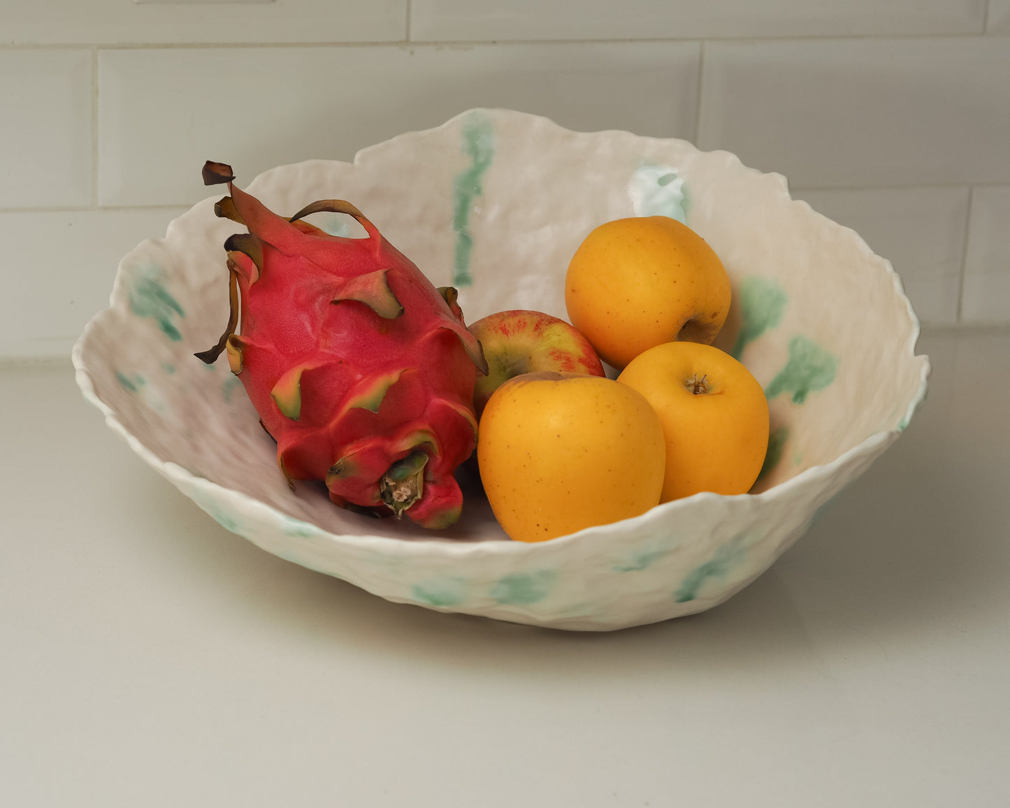 Fruit including a dragon fruit and oranges in a decorative bowl on a tiled wall background