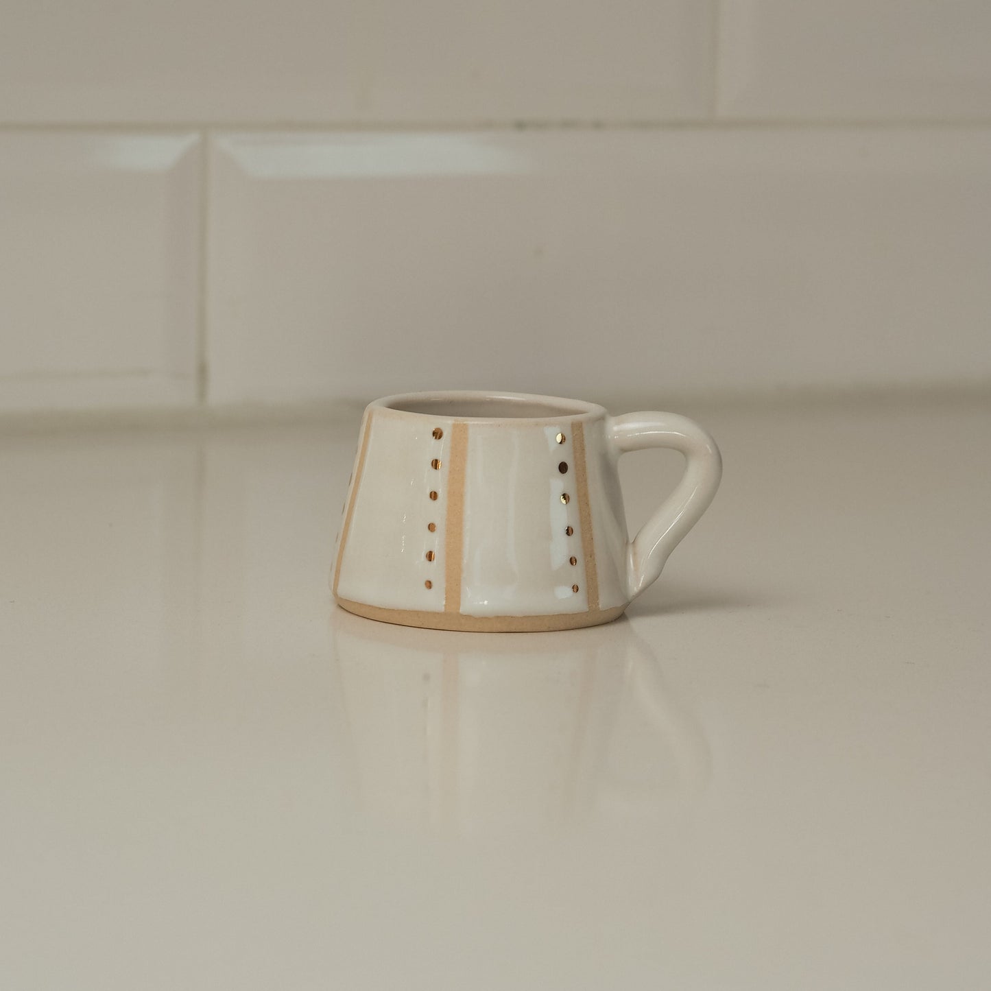 White ceramic mug with decorative elements on a light-colored surface with tiled wall background